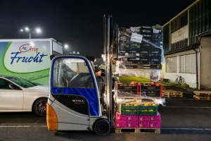 Ein STILL-Gabelstapler verlädt nachts frische Obst- und Gemüsekisten vor einem MK City Frucht Liefer-Lkw auf dem Großmarktgelände in Berlin.